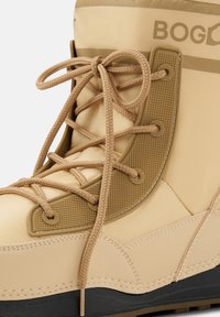 Beżowy wodoodporny but z teksturowanymi akcentami i grubymi sznurowadłami. Projekt obejmuje wyściełany kołnierz oraz czarną gumową podeszwę zapewniającą przyczepność.