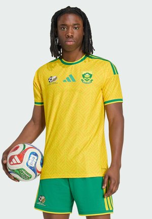 Nuori miesurheilija Etelä-Afrikan jalkapallopaidassa ja vihreissä shortseissa, joka pitää moniväristä FIFA:n jalkapallon MM-kisojen palloa.