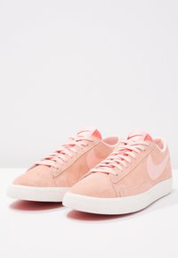 Rosa mockaskinnssneakers med en texturerad vit gummisula, som har en tonad rosa Nike-logotyp och matchande snören, minimalistisk design.