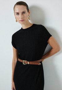 Abito nero a coste con maniche corte, stretto in vita da una cintura marrone con una fibbia dorata. Texture sottile e design aderente.