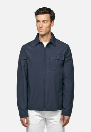 Giacca leggera navy con zip frontale, colletto a punta e tasca sul petto con bottone. Texture liscia e vestibilità su misura.