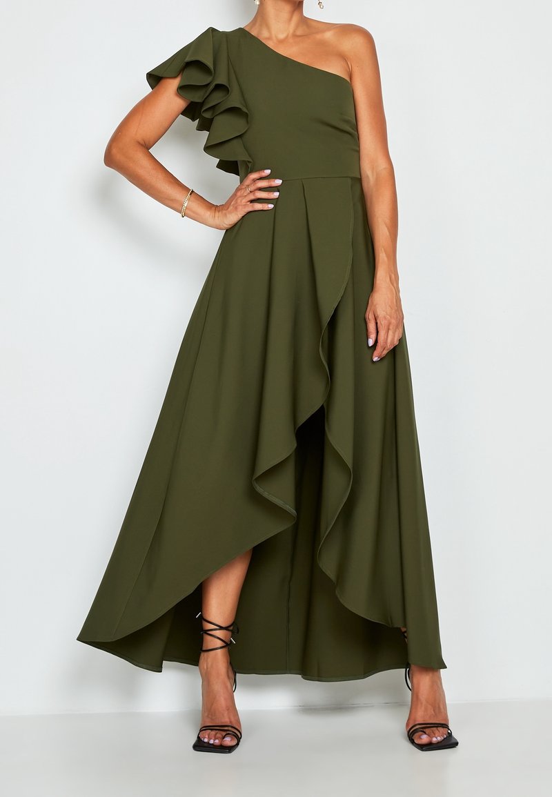 Robe olive verte à une épaule avec des détails de manche froncée et un devant en cascade. Présente une ourlet asymétrique et un tissu fluide. Sandales noires à talons avec lanières.