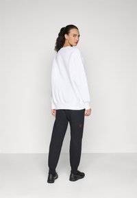 Hvitt sweatshirt med avslappet passform, sammen med mørkegrå joggebukser med en liten rød logo på venstre lår. Svarte joggesko.