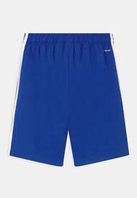 Modré sportovní šortky s elastickým pasem, vybavené bílými bočními pruhy a hladkým povrchem. Logo značky na zadní straně.