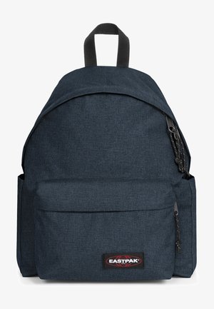 Mochila de tela azul oscura con forma redondeada, bolsillo frontal con cremallera, asa en la parte superior y parche del logo de la marca. Superficie texturizada con un diseño minimalista.