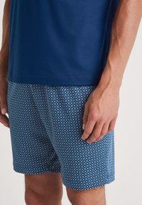 Blauwe T-shirt gecombineerd met gestreepte blauwe shorts met een geometrisch ontwerp in lichtere blauwtinten, met de nadruk op een lichtgewicht stof en een casual pasvorm.