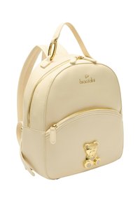Zaino in pelle beige con design arrotondato, accessori dorati, tasca frontale con cerniera e un ciondolo a forma di orsetto. Due spallacci regolabili.