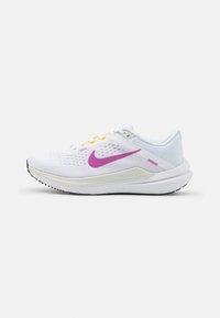 Zapatillas de running Nike con parte superior de malla blanca, swoosh púrpura, acentos amarillos y púrpuras, y una suela exterior de goma negra texturizada.