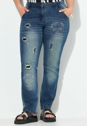 Džíny z denimu v středně modré barvě s opotřebovaným designem, který zahrnuje trhliny a vzor lebky dozdobený nýty. Rovný střih.