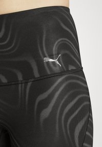 Svarta leggings med ett subtilt vågmönster, tillverkade av stretchigt tyg. Har en silverfärgad Puma-logotyp och kontrasterande sömmar.