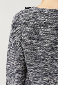 Kurzarmpullover aus blau-weiß gemustertem Strickstoff, mit einem einfachen runden Ausschnitt und strukturierten Schulterdetails.