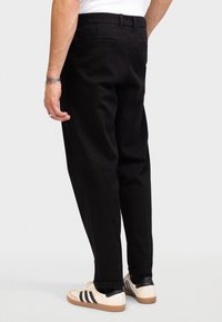 Black pants with a relaxed fit, featuring belt loops and two back pockets. Paired with cream and black sneakers for contrast.