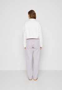 Chaqueta blanca cortada con detalles de ojales, combinada con pantalones de tiro alto en lavanda claro, que presentan un diseño de pierna recta y un estilo minimalista.