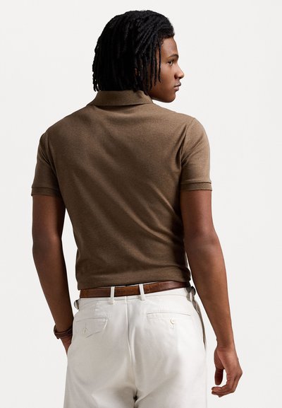 Camisa polo castanha com colarinho, mangas curtas e um design ajustado. Combinada com calças de cor clara e um cinto castanho. Textura simples.