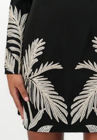 Black dress featuring intricate silver palm leaf embroidery, with long sleeves and a fitted silhouette, showcasing textured details and patterns.