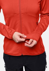 Giacca con zip rossa caratterizzata da un motivo testurizzato. Presenta maniche lunghe e fori per i pollici. Sono visibili zip nere e accenti sui taschini.