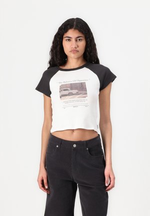 Cotton crop top with black raglan sleeves, featuring a printed graphic and text design on the front. Paired with high-waisted black pants.