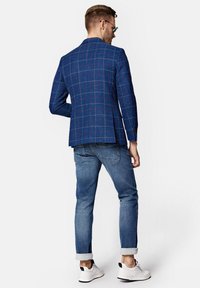 Niebieska blazer z kratą i czerwonymi akcentami, o teksturowanej tkaninie, w połączeniu z podwiniętymi jasnoniebieskimi jeansami i białymi trampkami.