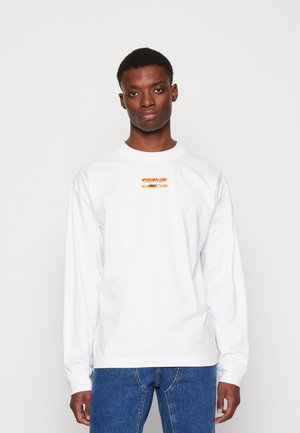 Bílý dlouhý rukáv tričko s malým obdélníkovým oranžovým logem s nápisem "Calvin Klein Jeans" na hrudi. Standardní střih, bavlněný materiál.