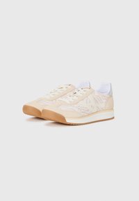 Une paire de baskets beiges et blanches avec un motif animal léger, des lacets blancs et des semelles couleur gomme sur fond blanc.