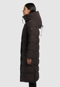 Manteau rembourré noir avec un col montant et une capuche réglable, présentant des coutures horizontales et des poches zippées sur les côtés, design longueur genou.