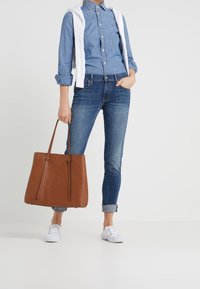 Camisa de mezclilla, chaleco de punto blanco, jeans azul oscuro, bolsa de mano marrón y zapatillas blancas. Enfoque en las texturas y los colores contrastantes de las telas.