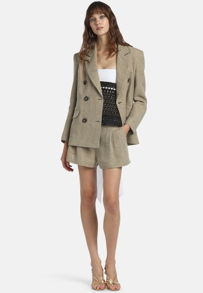 Bézs len kétsoros blézer fekete horgolt felsőrésszel, fehér aláöltéssel és hozzáillő bézs rövidnadrággal. Arany pántos szandál.