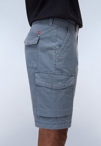 Cargo shorts in light gray fabric with multiple pockets, a patch detail, stitched seams, and a casual, relaxed fit.