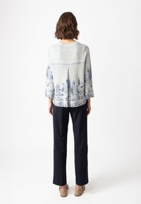 Light gray top with blue landscape pattern, three-quarter sleeves, back pleat detail, paired with black trousers and tan flats.