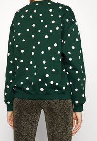 Sudadera verde con lunares blancos, cuello redondo, y ribetes en el bajo y los puños. Combinada con leggins dorados brillantes y texturizados.