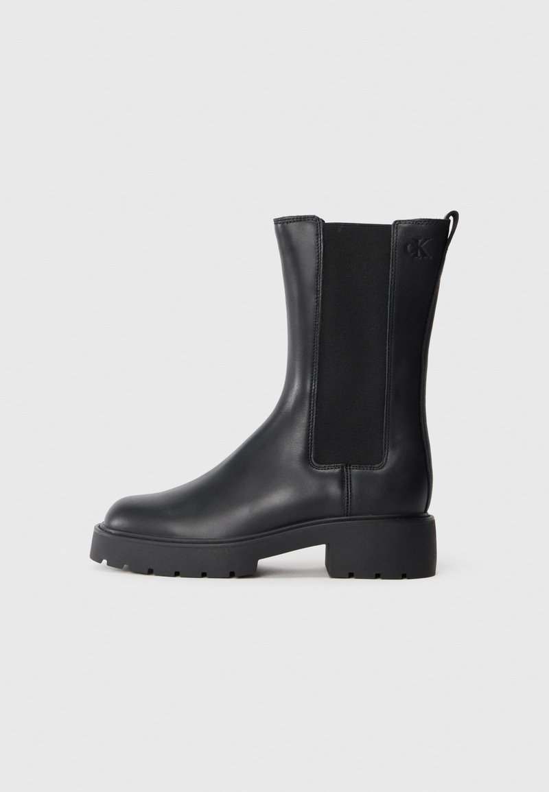Botte noire en cuir mi-mollet avec semelle épaisse, panneau latéral élastique, languette de traction au talon et petit logo "cK" embossé près du haut.