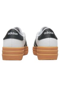 Zapatillas blancas de cuero con acentos negros y tres rayas, que cuentan con una gruesa suela de goma y el logotipo "adidas" en el talón.