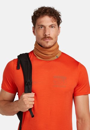 Pomarańczowa krótko rękawowa koszula o teksturowanym wzorze i okrągłym dekolcie, w połączeniu z beżowym kominem na szyję. Widoczny jest czarny pasek od plecaka.