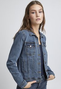 Jeans jakna u srednje plavoj boji, s klasičnom kragnom, dugmadi na kopčanje, dva džepa na grudima i bočnim džepovima. Tekstuirana tkanina s vidljivim šavovima.