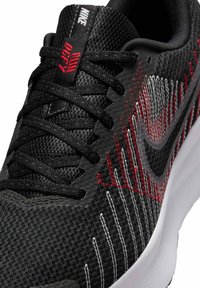 Schwarzer Nike Sport Schuh mit einem Obermaterial aus Mesh; verfügt über rote und weiße Streifen, dicke Schnürsenkel und eine weiß gepolsterte Sohle.