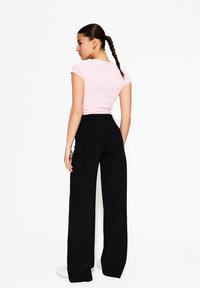 Haut rose ajusté à manches courtes associé à un pantalon large noir taille haute, sur fond blanc uni.