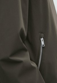 Nærbillede af mørkt stof med en sølvfarvet metallynlås, delvist lukket på højre side.