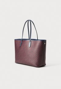 Sac fourre-tout rouge et marine avec un motif géométrique, dotée de longues anses fines et d'une forme rectangulaire structurée. Matériau synthétique texturé.