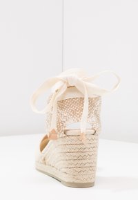 Beige espadrille-hæl med et vævet mønster, satin ankelbånd og en struktureret jute hæl. Har et åbent hæl-design og polstret sål.