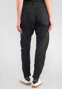 Zwarte cargobroek met een ontspannen pasvorm, voorzien van grote achterzakken en taps toelopende benen. De stof is soepel met een matte afwerking, geschikt voor casual gebruik.