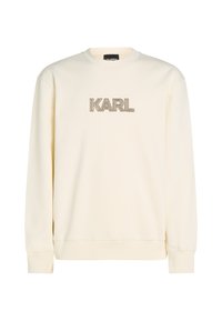 Cremefarvet sweatshirt med rund hals og lange ærmer. Har ordet "KARL" i en gylden, dekorativ skrifttype på fronten.