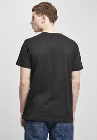 Svart bomull T-skjorte med rund hals og korte ermer, vist fra baksiden, sammen med blå denimjeans.