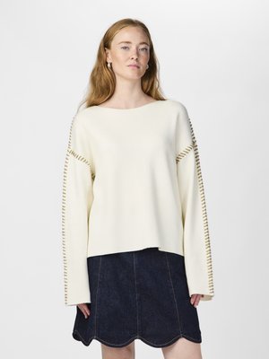 Pull crème à manches larges avec un détail de couture contrasté. Associé à une jupe en denim foncé avec un ourlet festonné.