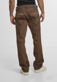 Jeans de mezclilla marrones con un corte recto, que cuentan con dos bolsillos traseros con costuras en contraste y una etiqueta de marca negra en la cinturilla.