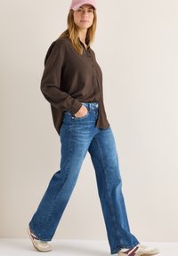 Braunes Hemd mit Knöpfen, blaue weite Jeans, hellfarbene Sneakers und eine rosa Cordmütze. Einfaches, lässiges Design mit entspannter Passform.