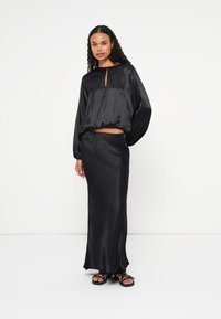 Top din satin negru cu decolteu rotund și detaliu tip cheie, asortat cu o fustă maxi din satin, având o textură netedă și o siluetă ajustată.