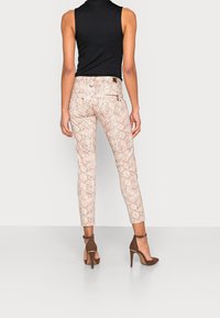 Růžové kalhoty s hadím potiskem a přiléhavým střihem, s mírně zvýšeným pasem a kapsami na zip. V kombinaci s hnědými vysokými podpatky.