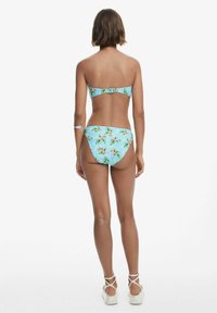 Két részes bikini világoskék háttérrel, trópusi virágmintázattal. A felső pánt nélküli, hátul csattal záródik; az alsó rész mérsékelt takarást biztosít.