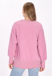 Felpa rosa in pile con polsini e orlo a coste, caratterizzata da una vestibilità rilassata e una trama morbida. Appare accogliente e casual nel design.