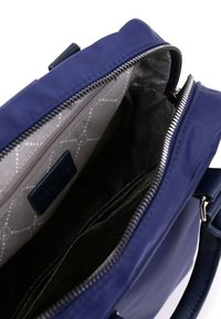 Mörkblå handväska med öppen dragkedja som visar gråmönstrad inredning och inre fickor, med silverfärgade dragkedjespår och ett läderhandtag.